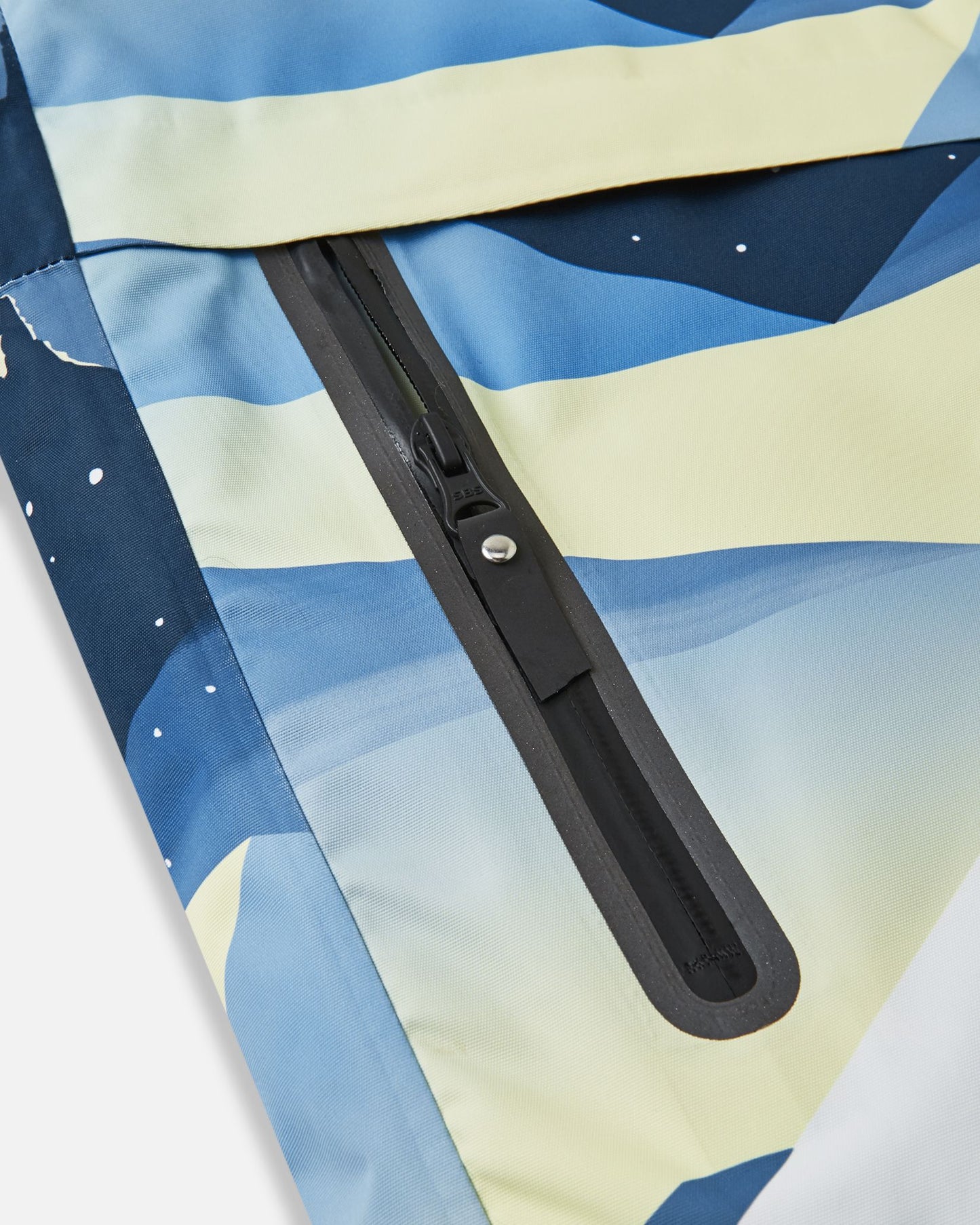 Close-up of the sealed, waterproof zippered side pocket on the ocean blue Reima Tirro kids' ski jacket, highlighting the durable and weather-resistant construction.