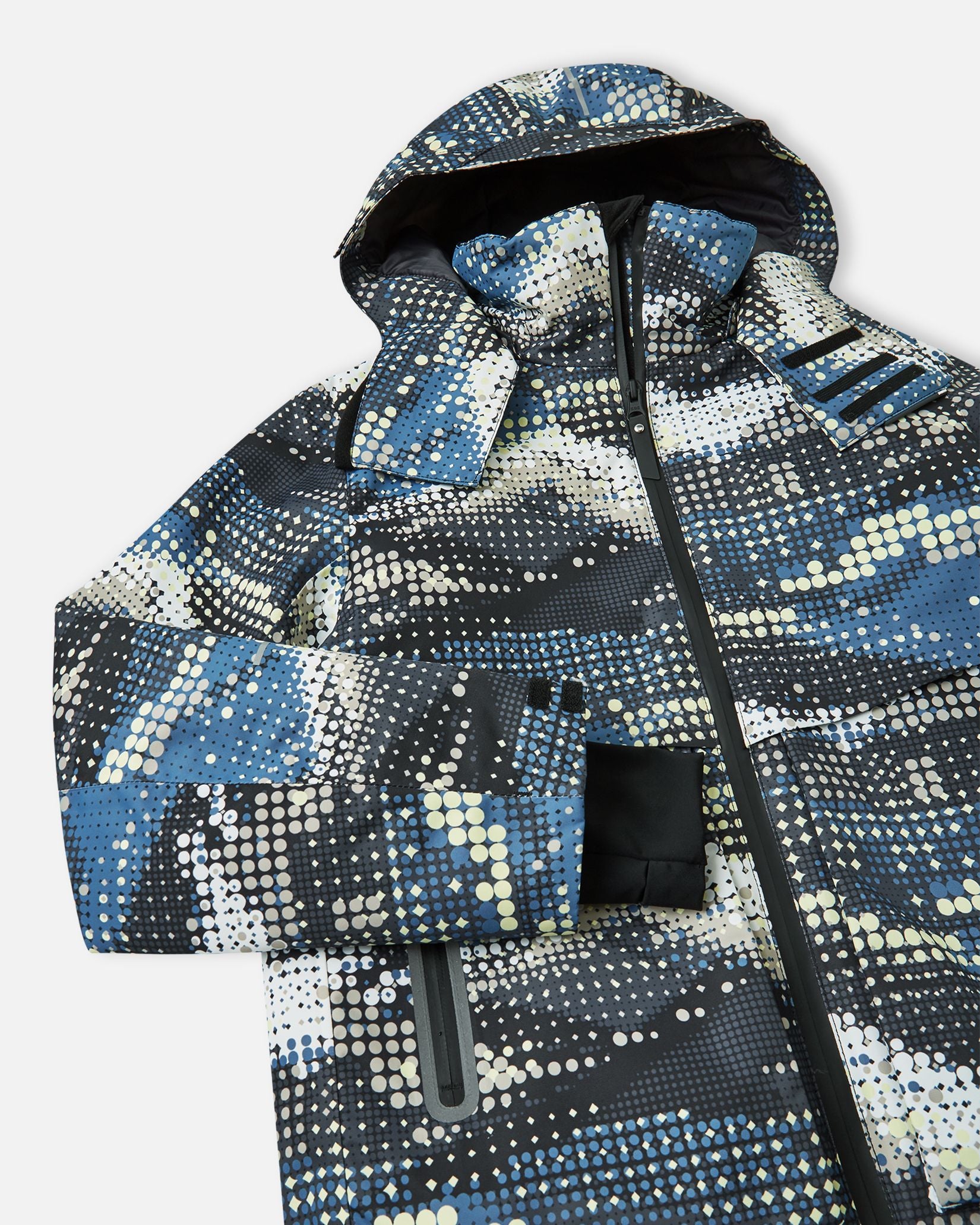Angled close-up of the upper chest, hood, and sleeve on the soft black Reima Tirro kids' waterproof ski jacket, showcasing the digital dot pattern and sealed front zipper.