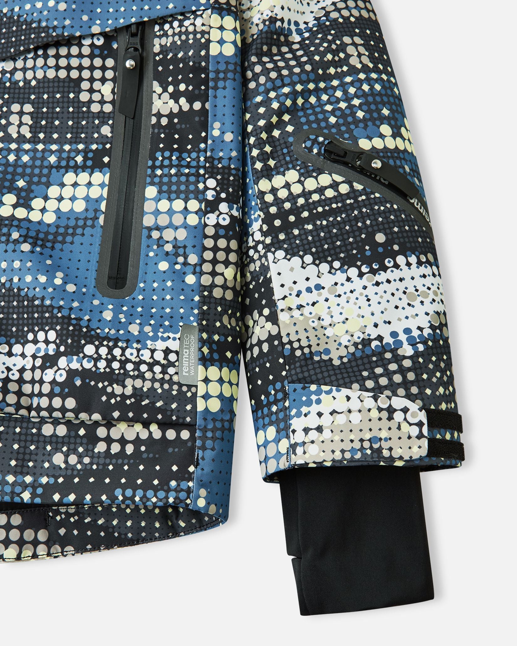 Close-up of the lower sleeve on the soft black Reima Tirro kids' ski jacket, highlighting the waterproof zippered ski pass pocket, adjustable velcro cuff, and inner lycra thumbhole cuff.