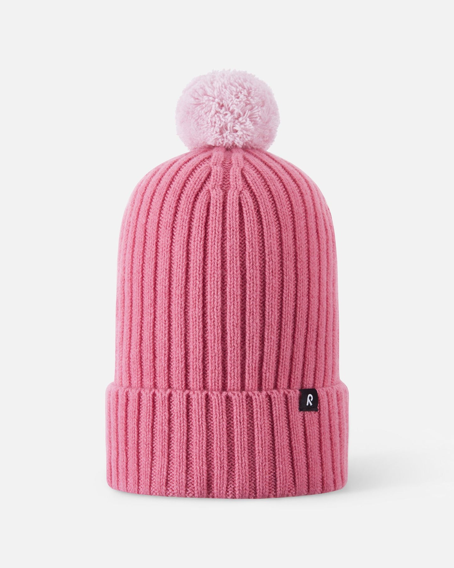 Front flat lay view of the soft coral pink Reima Topsu kids' winter beanie. The image highlights the warm ribbed knit texture, a wide folded brim for extra ear protection, and a matching playful yarn pom-pom on top.