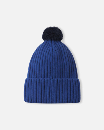 Back flat lay view of the twilight blue Reima Topsu kids' wool blend beanie, displaying the continuous stretchy ribbed knit pattern and the cozy navy pom-pom designed to retain heat on cold days.