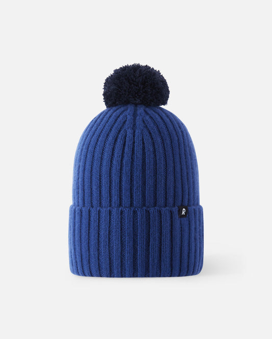Front flat lay view of the twilight blue Reima Topsu kids' winter beanie. The image highlights the deep blue vertical ribbed knit texture, a wide folded brim, and a contrasting navy dark blue yarn pom-pom on top.