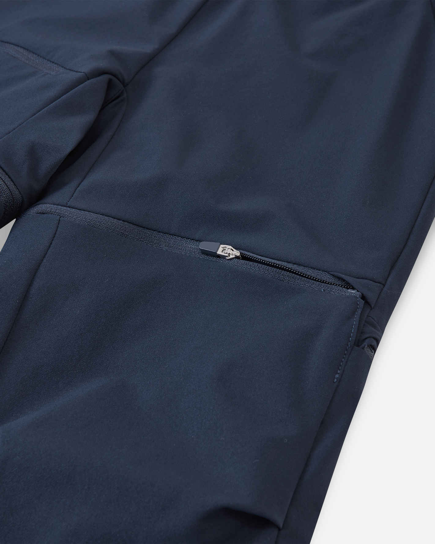 Macro close-up of the hidden zipper detail on the Reima Tuplat kids' navy blue convertible hiking pants, showcasing the smooth, high-quality zipper hardware used to detach the lower pant legs and easily convert them into shorts.