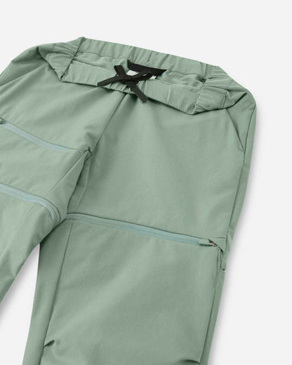 Close-up view of the upper front on the Reima Tuplat kids' stone green hiking pants, detailing the flexible elastic waistband with a secure black inner drawstring, side pockets, and the concealed zipper for detaching the lower pant legs.