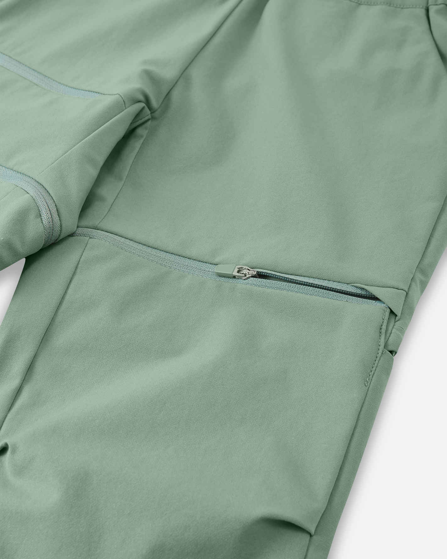 Detailed close-up of the concealed zip-off leg attachment on the Reima Tuplat kids' stone green convertible pants, highlighting the durable stitching and easy-to-use zipper designed for quick conversion during outdoor hikes.