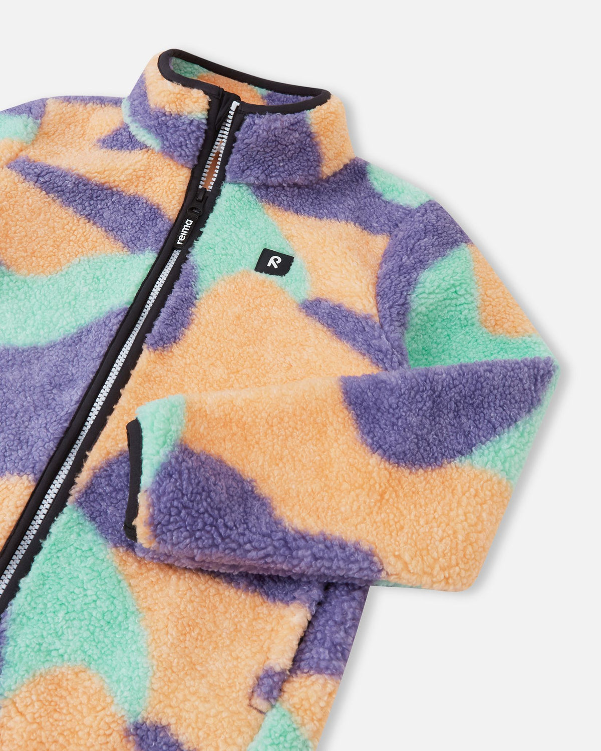 Close-up of the upper section of the apricot Reima Tupsis kids' teddy fleece, detailing the reliable full zipper, cozy collar, bound cuffs, and the signature Reima chest logo.