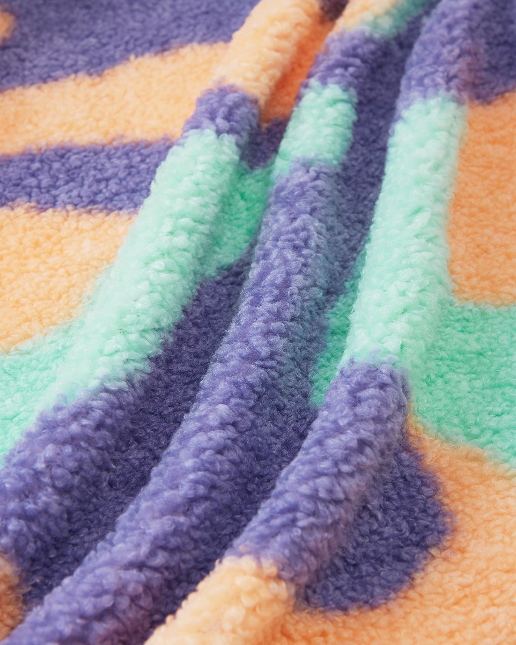 Macro close-up of the ultra-soft, thick teddy fur fleece used on the apricot Reima Tupsis kids' jacket, highlighting the plush texture and the bright orange, purple, and mint green camo pattern designed for cozy winter layering.