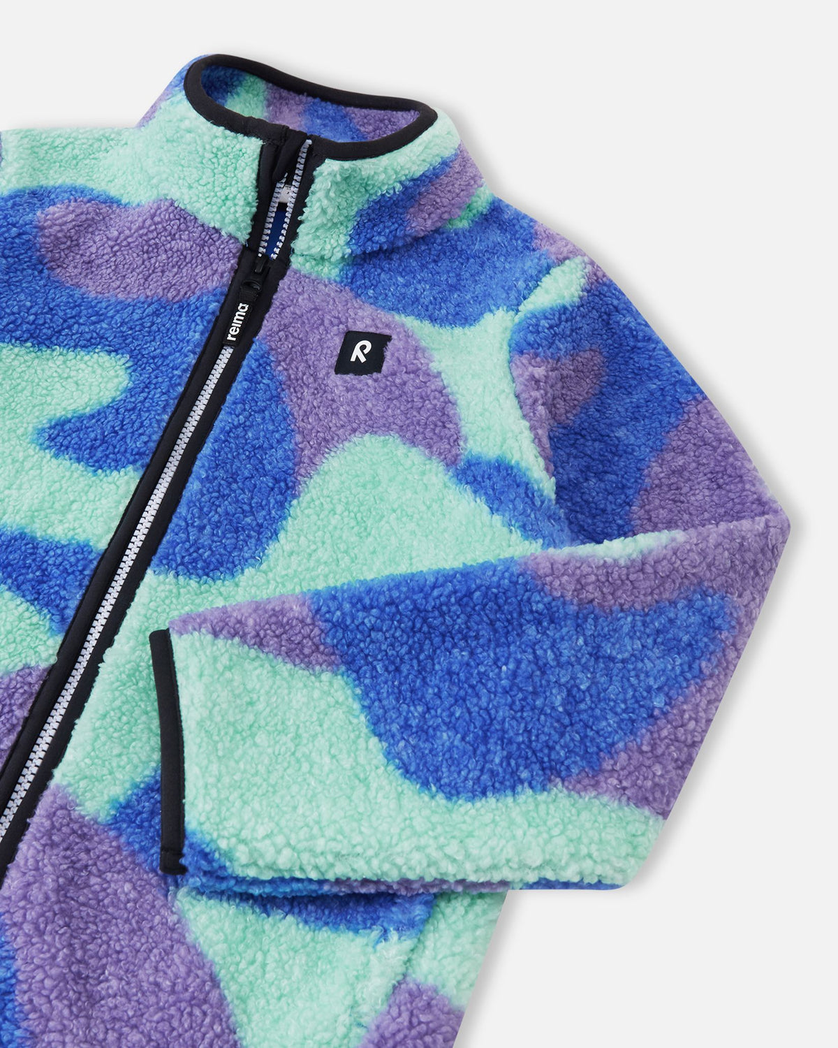 Close-up of the upper front on the sparkly blue Reima Tupsis kids' fleece jacket, highlighting the sturdy front zipper, protective high collar, soft teddy fabric, and the small black Reima logo patch.