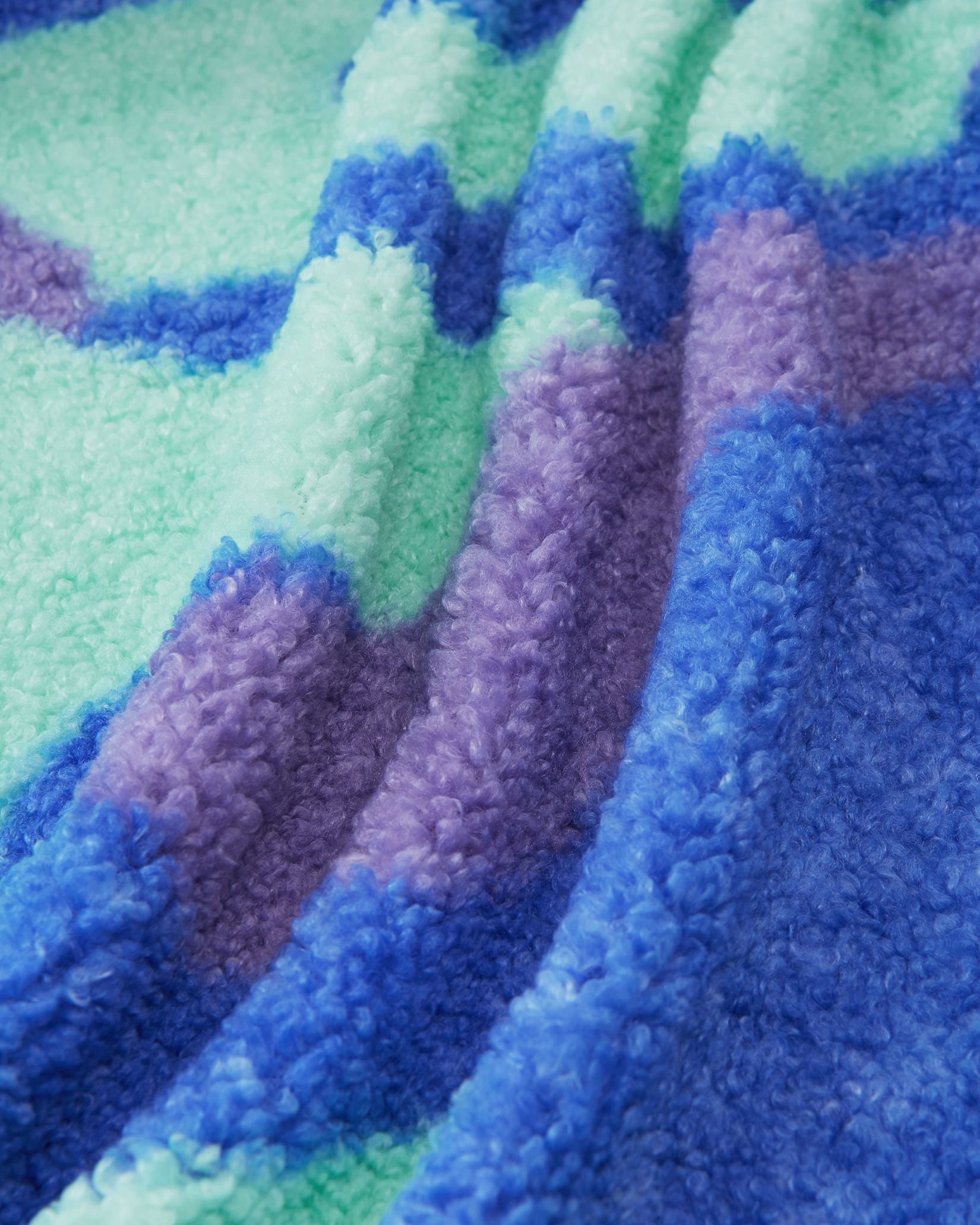 Macro close-up of the ultra-soft, thick teddy fur fleece used on the sparkly blue Reima Tupsis kids' jacket, showing the rich texture and vibrant colors of the camo pattern.