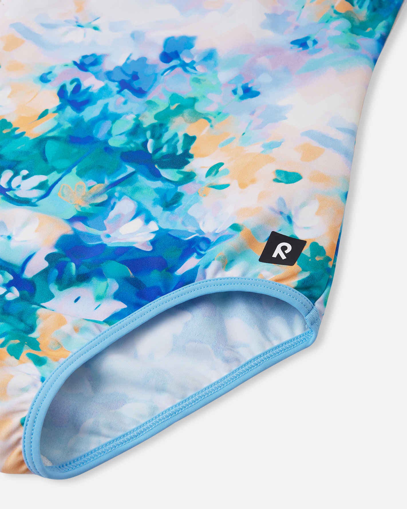 Detailed close-up of the Reima Uimaan girls' cool blue watercolor swimsuit, focusing on the soft, quick-drying stretch fabric, light blue elastic leg binding, and the signature Reima logo tag.