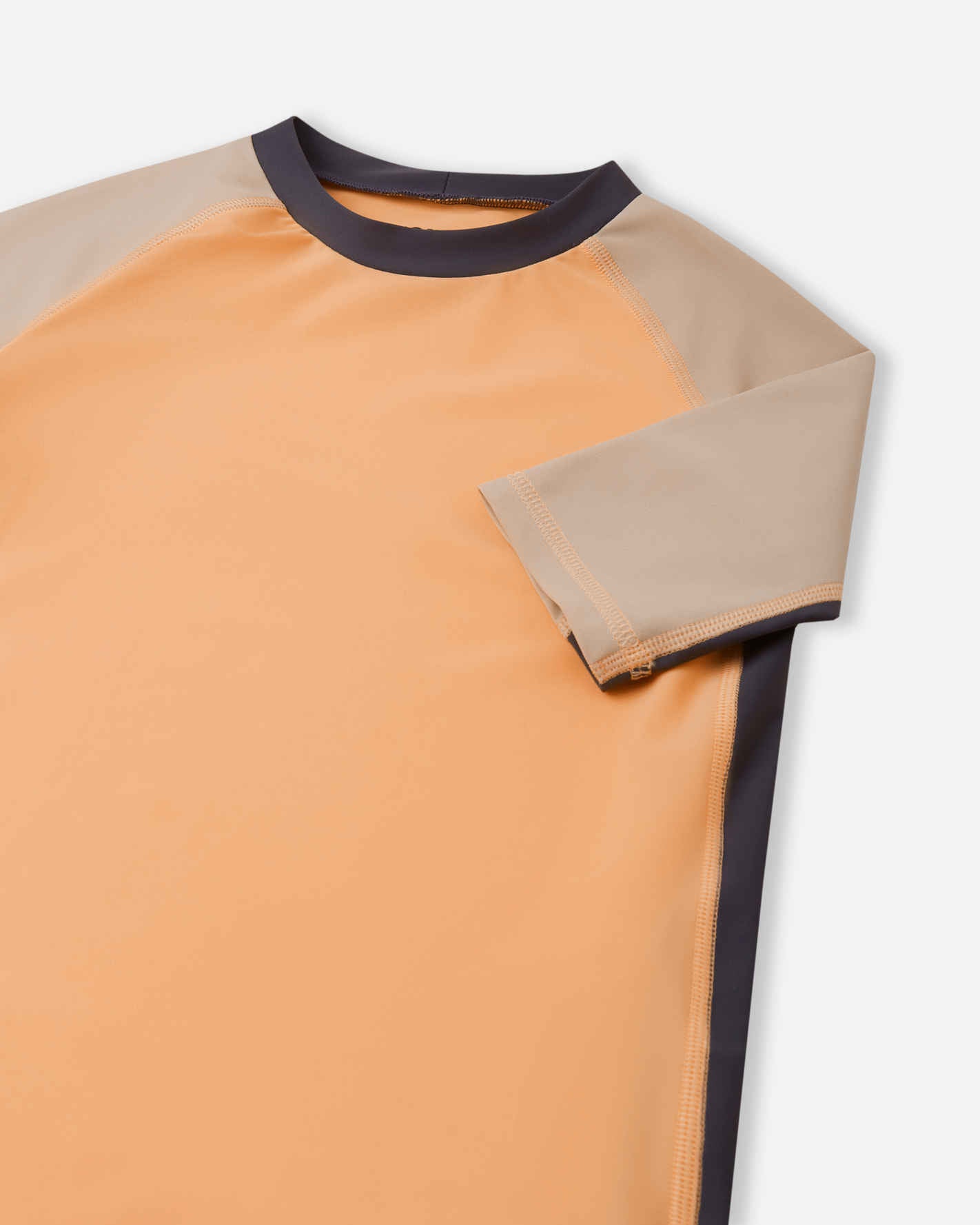 Detailed close-up of the Reima Uiva kids' apricot sunproof rash guard, focusing on the beige short sleeve, smooth flatlock stitching, and the comfortable stretch-knit collar designed to keep its shape.