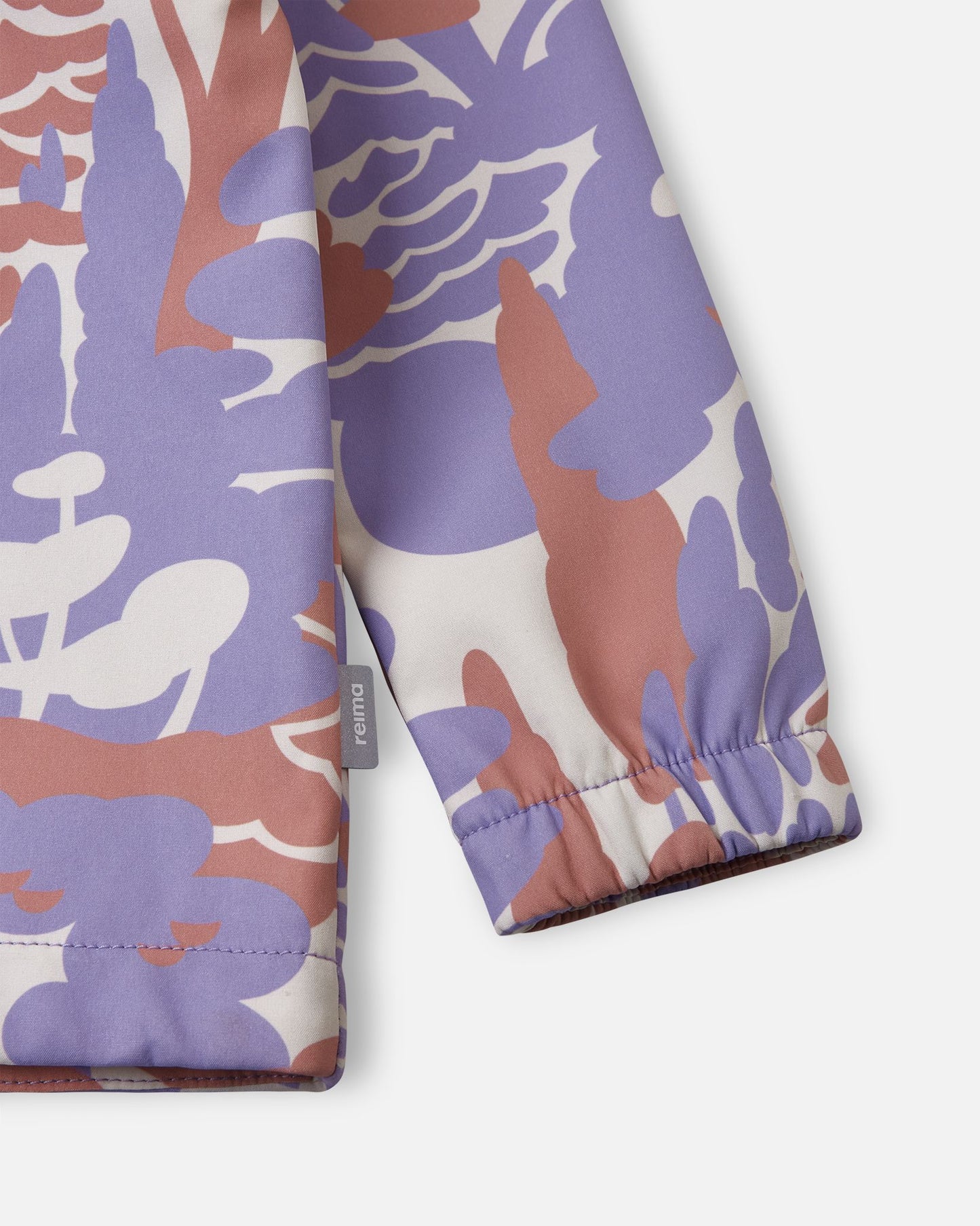 Detailed close-up of the sleeve on the blooming lilac Reima Vantti kids' softshell jacket, highlighting the bold forest print, the small Reima logo side tag, and the snug elastic cuff that seals out the elements.