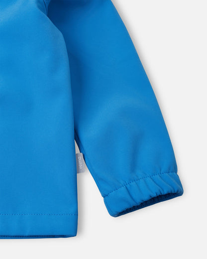 Detailed close-up of the sleeve on the cool blue Reima Vantti kids' softshell jacket, highlighting the durable windproof fabric, the small Reima logo side tag, and the snug elastic cuff that seals out the elements.