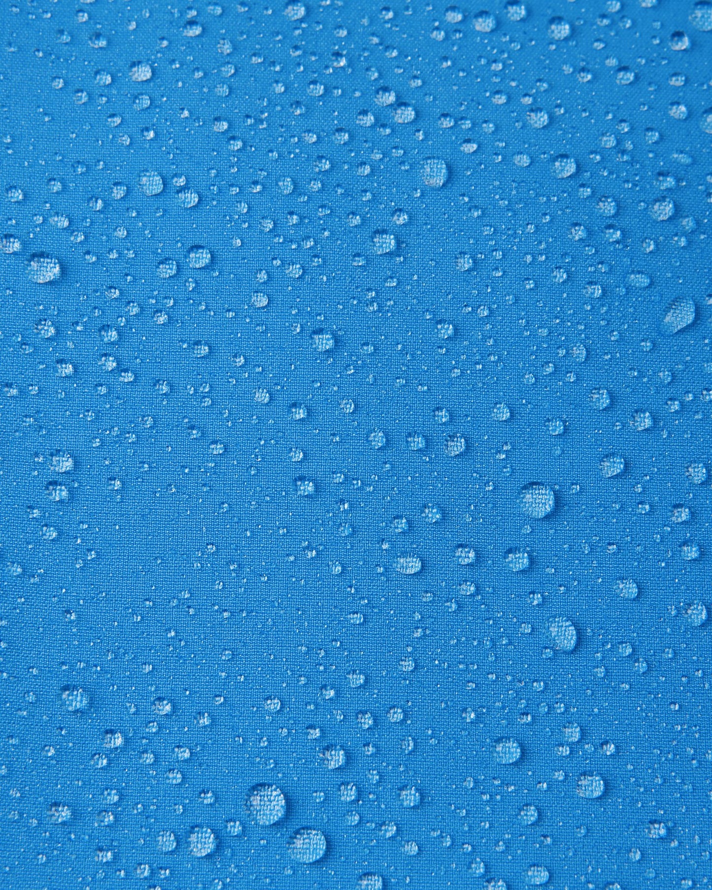 Macro close-up of water droplets beading and rolling off the surface of the Reima Vantti kids' cool blue softshell jacket, demonstrating the highly waterproof and dirt-repellent material.