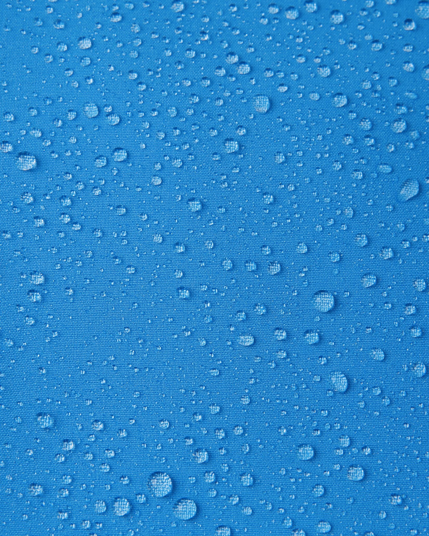 Macro close-up of water droplets beading and rolling off the surface of the Reima Vantti kids' cool blue softshell jacket, demonstrating the highly waterproof and dirt-repellent material.