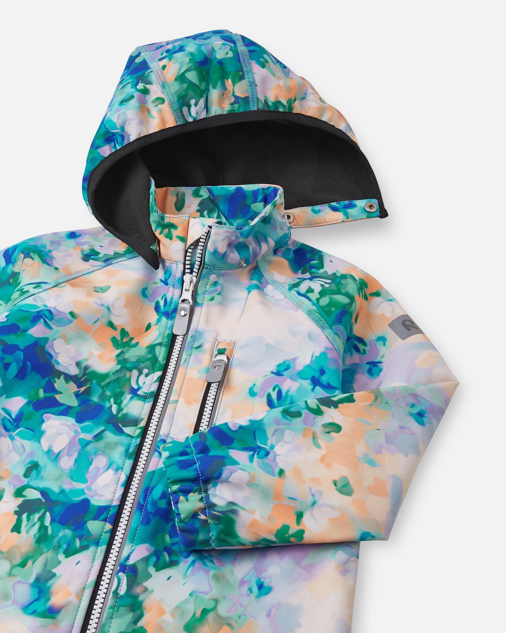 Close-up of the hood and high collar on the fresh blue floral Reima Vantti kids' softshell jacket, showing the cozy, insulating black fleece lining that provides extra warmth without bulk.