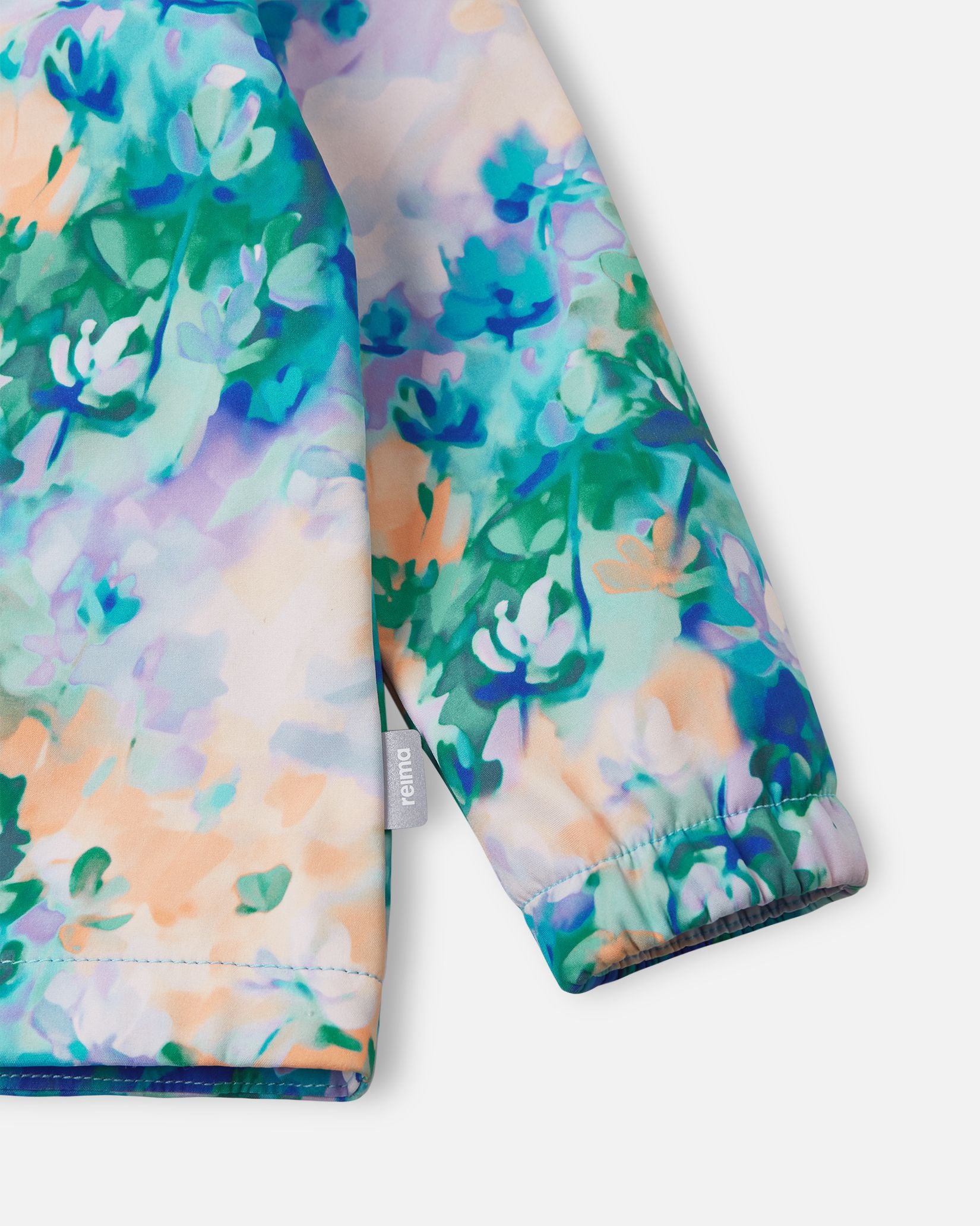 Detailed close-up of the sleeve on the fresh blue floral Reima Vantti kids' softshell jacket, highlighting the vibrant print, the small Reima logo tag, and the snug elastic cuff designed to keep the wind out.