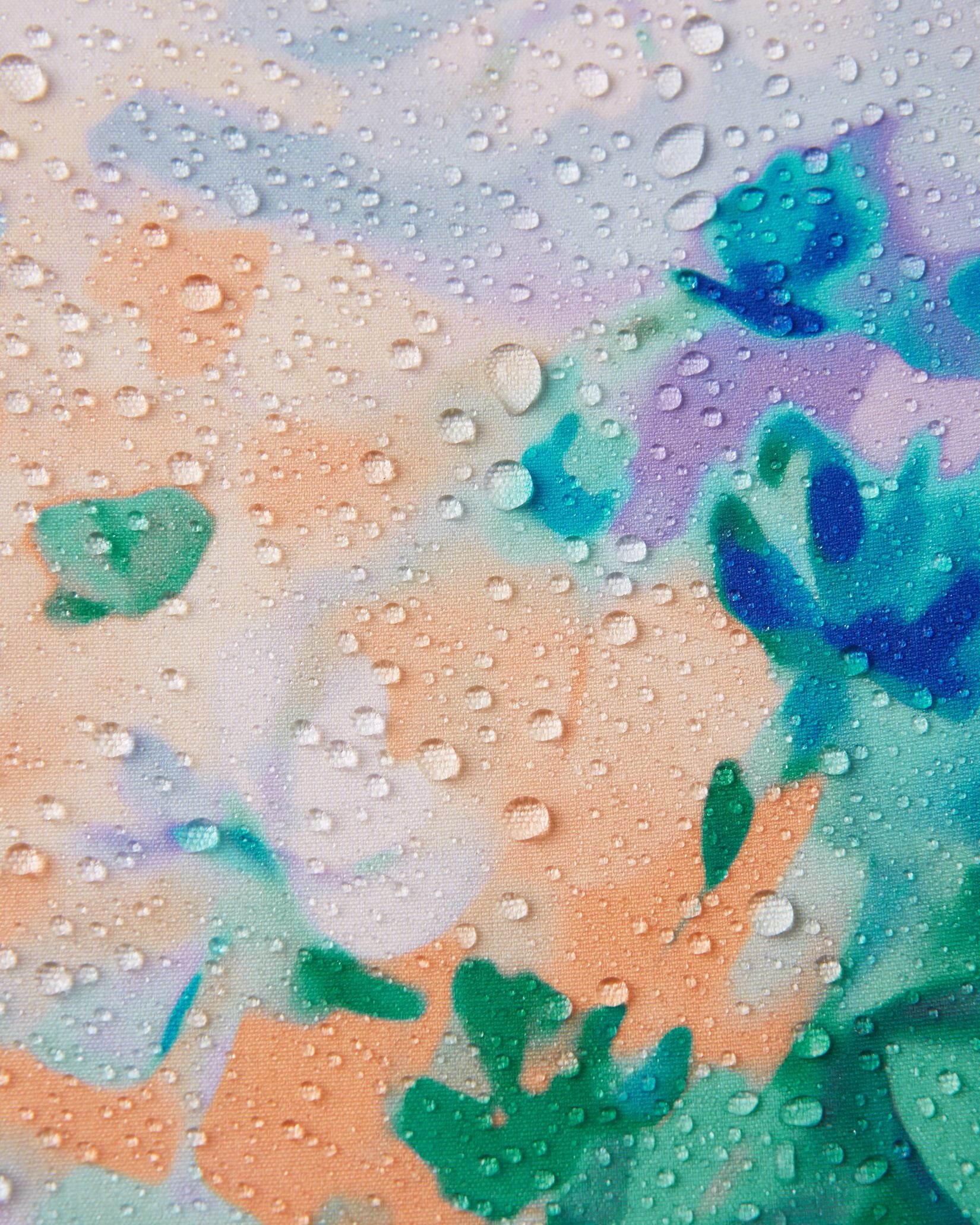 Macro close-up of water droplets beading and rolling off the surface of the Reima Vantti kids' fresh blue floral softshell jacket, demonstrating the highly waterproof and dirt-repellent material.