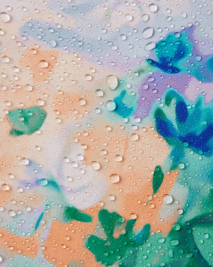 Macro close-up of water droplets beading and rolling off the surface of the Reima Vantti kids' fresh blue floral softshell jacket, demonstrating the highly waterproof and dirt-repellent material.