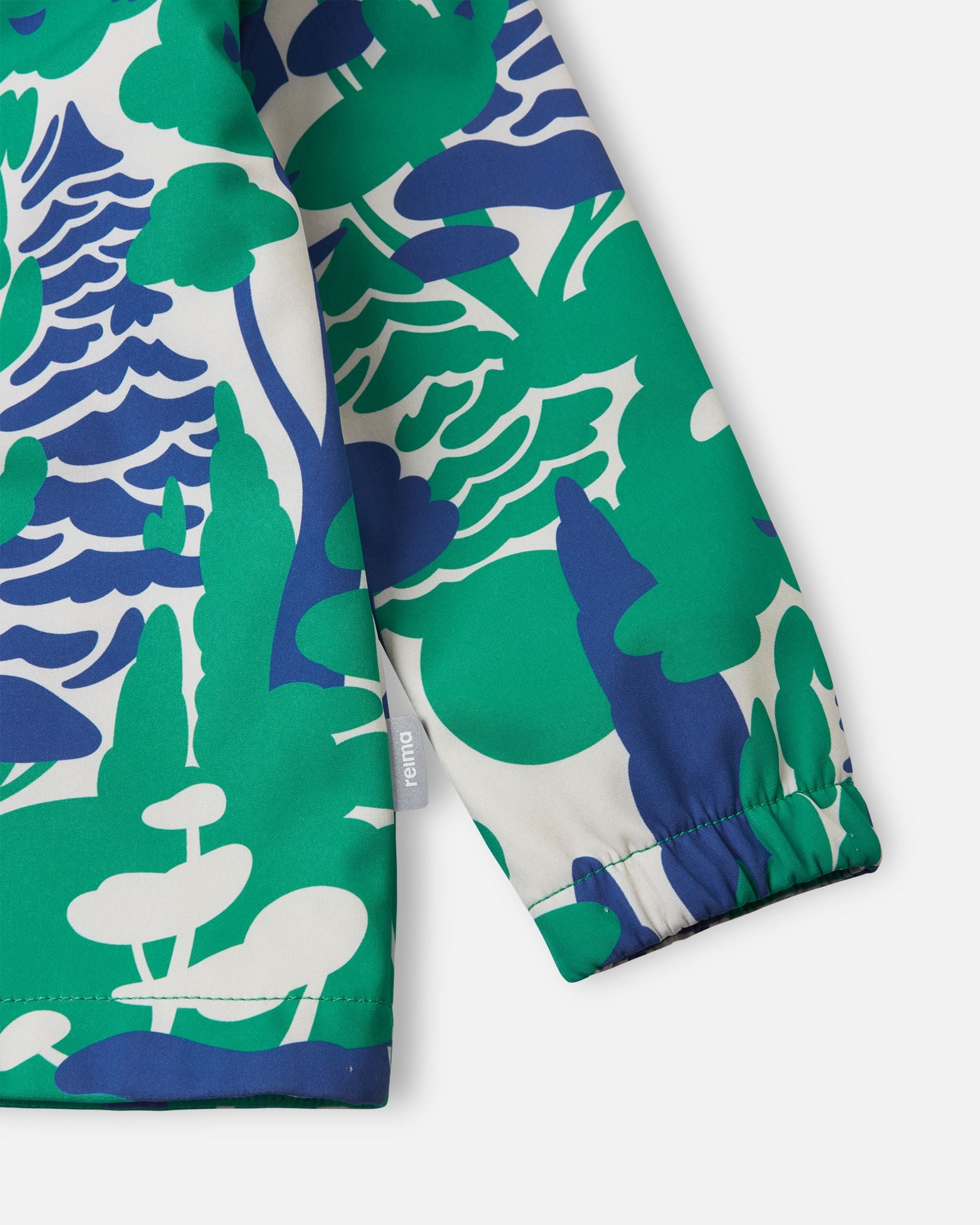 Detailed close-up of the sleeve on the green Reima Vantti kids' softshell jacket, highlighting the bold forest print, the small Reima logo tag, and the snug elastic cuff that seals out wind.