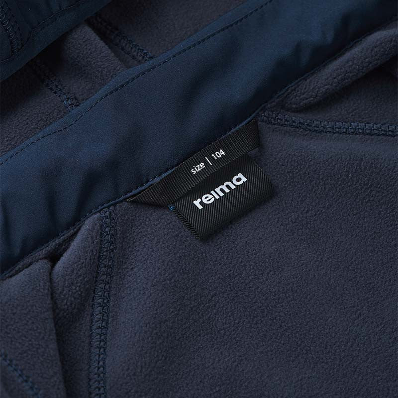 Inside view of the Reima Vantti kids' softshell jacket collar, displaying the Reima size 104 label and the soft, brushed navy fleece interior that provides breathable warmth.