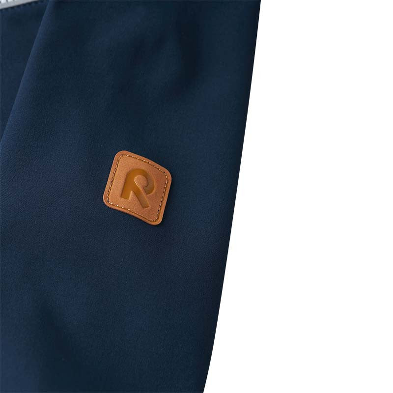 Close-up of the upper sleeve on the navy Reima Vantti kids' softshell jacket, featuring the signature brown faux-leather Reima 'R' logo patch detailing.