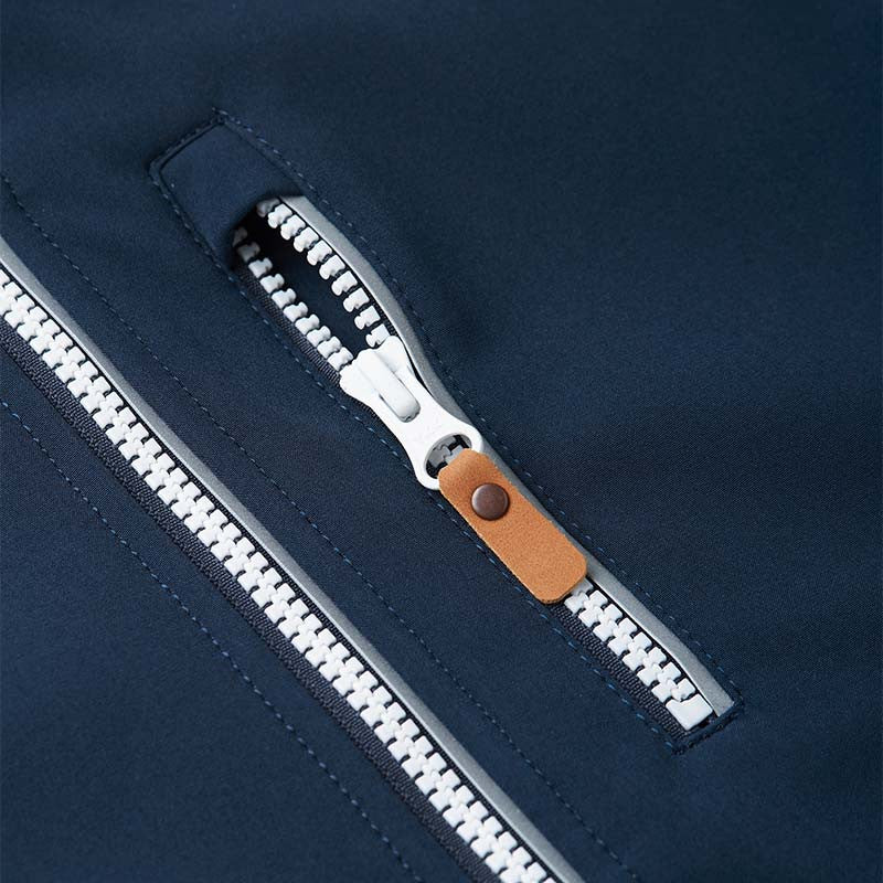 Detail shot of the functional zippered chest pocket on the Reima Vantti kids' navy softshell jacket, featuring a stylish brown faux-leather zipper pull set against the durable water-repellent fabric.