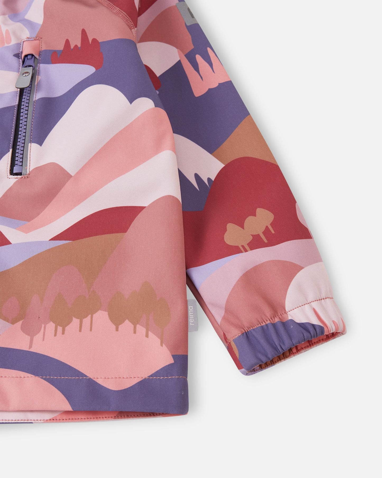 Detailed close-up of the lower body and sleeve on the rose blush Reima Vantti kids' softshell jacket, focusing on the vibrant mountain print, side logo tag, and snug wind-blocking elastic cuff.