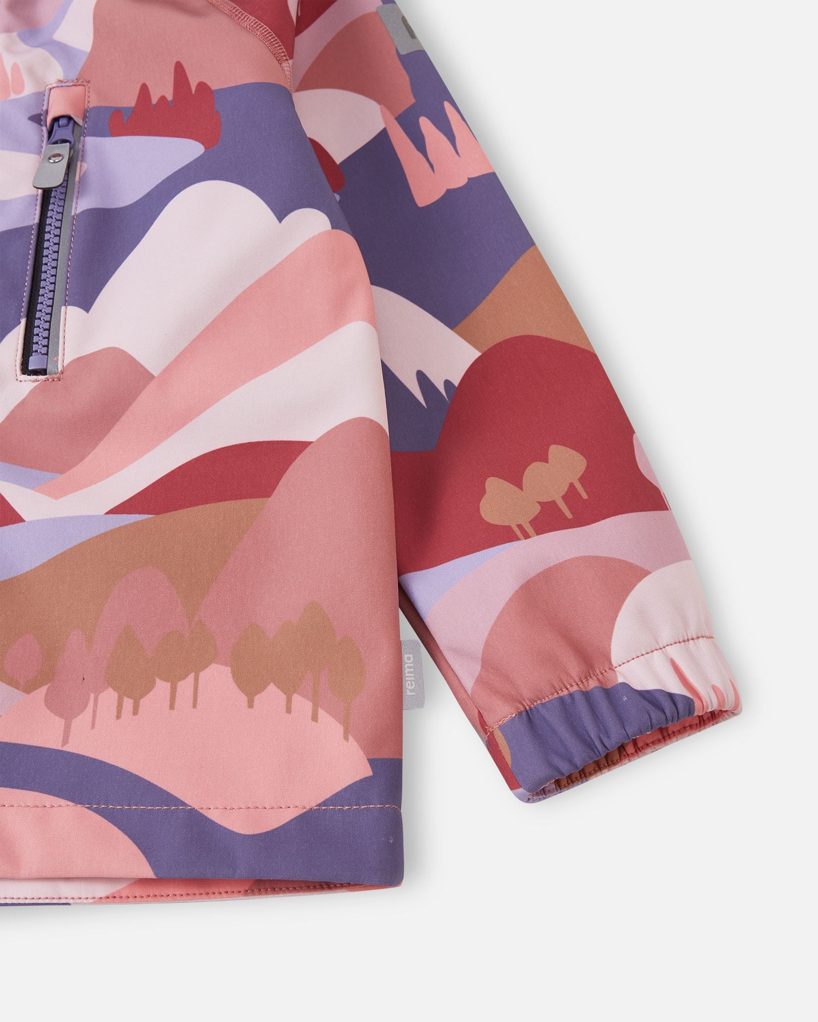 Detailed close-up of the lower body and sleeve on the rose blush Reima Vantti kids' softshell jacket, focusing on the vibrant mountain print, side logo tag, and snug wind-blocking elastic cuff.