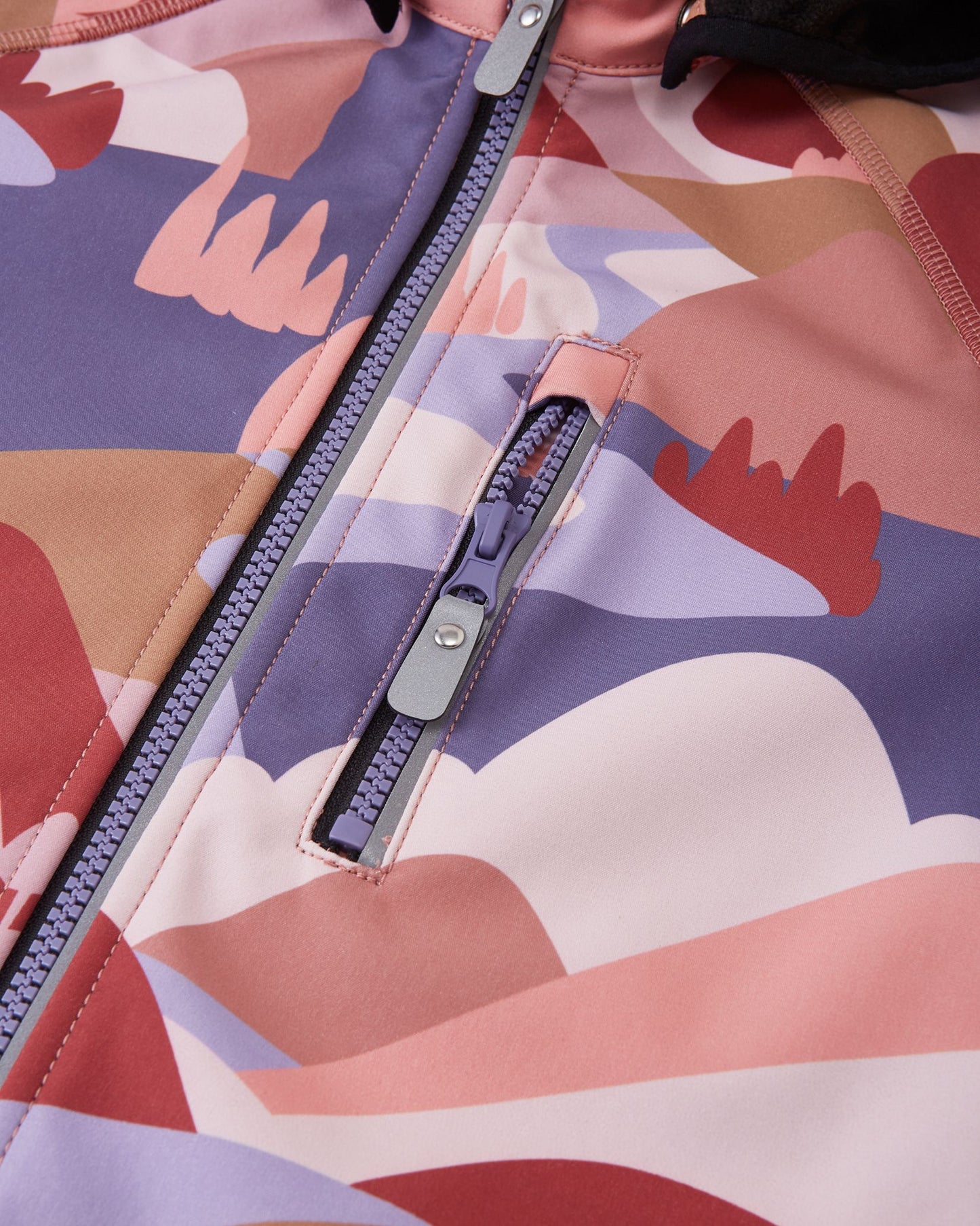 Close-up view of the zippered chest pocket on the Reima Vantti kids' rose blush softshell jacket, featuring a purple zipper pull and durable water-repellent finish.