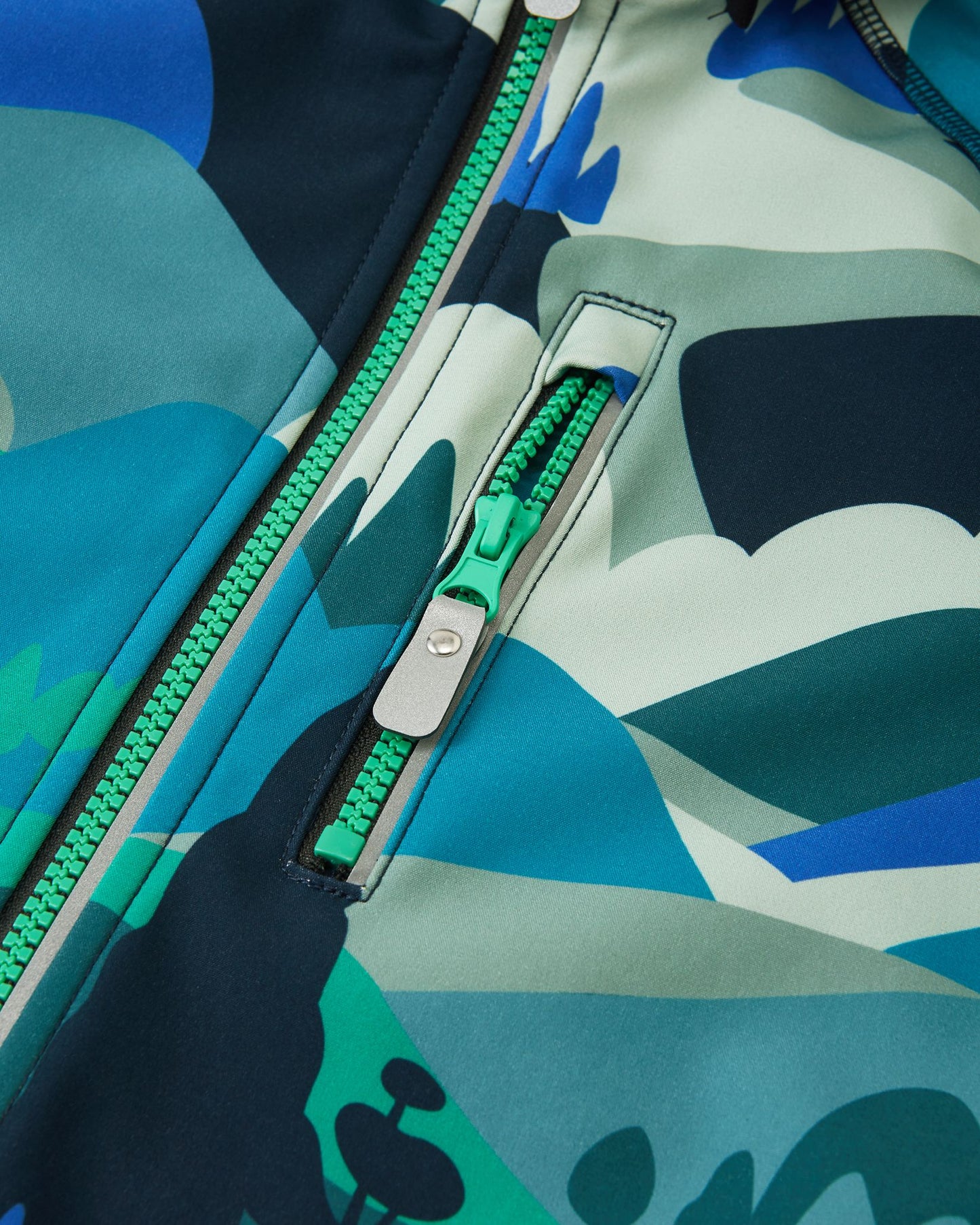 Close-up view of the zippered chest pocket on the Reima Vantti kids' sparkly blue softshell jacket, featuring a color-matched green zipper and durable water-repellent finish.