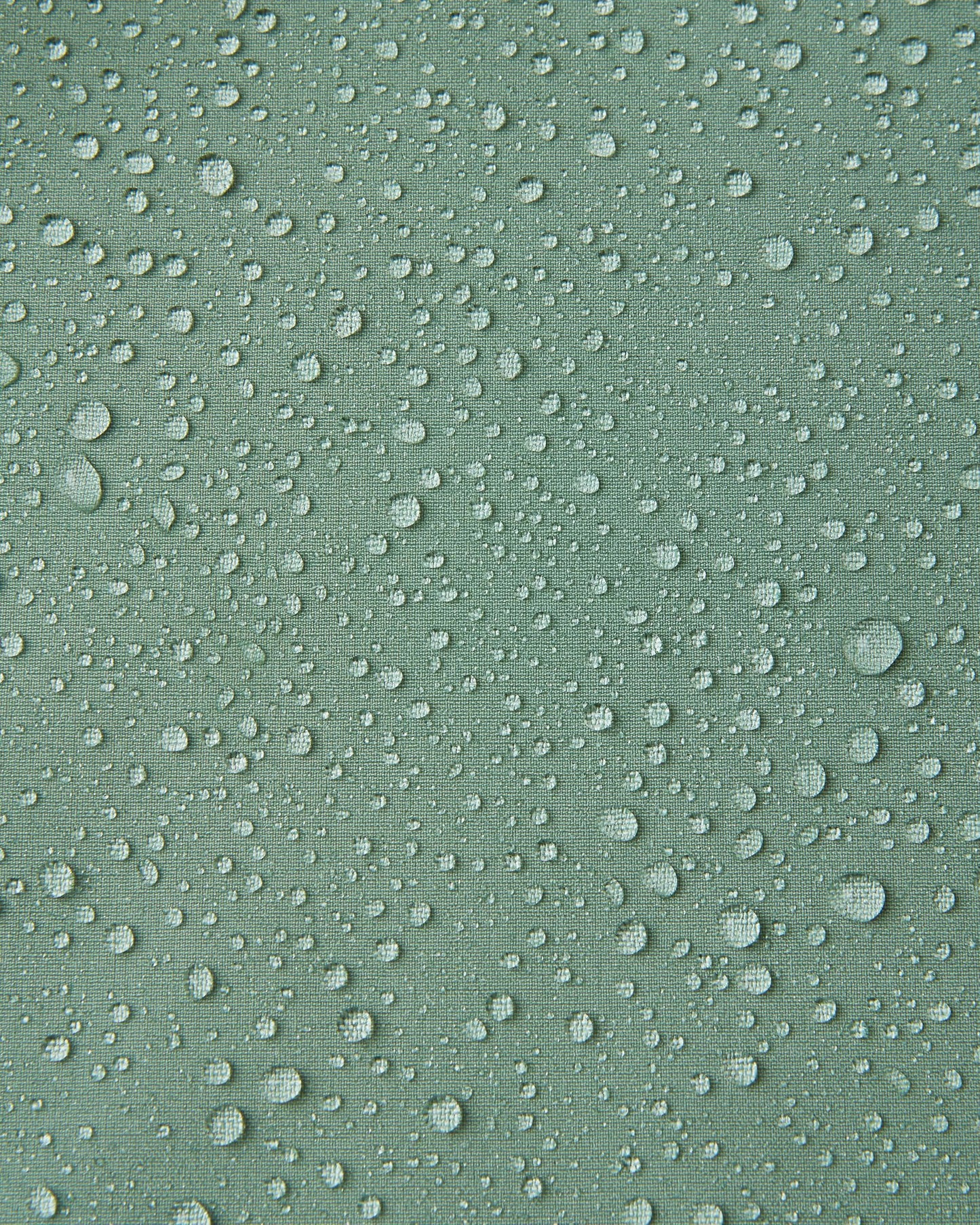 Macro close-up of water droplets beading and rolling off the surface of the Reima Vantti kids' stone green softshell jacket, demonstrating the highly waterproof and dirt-repellent material.