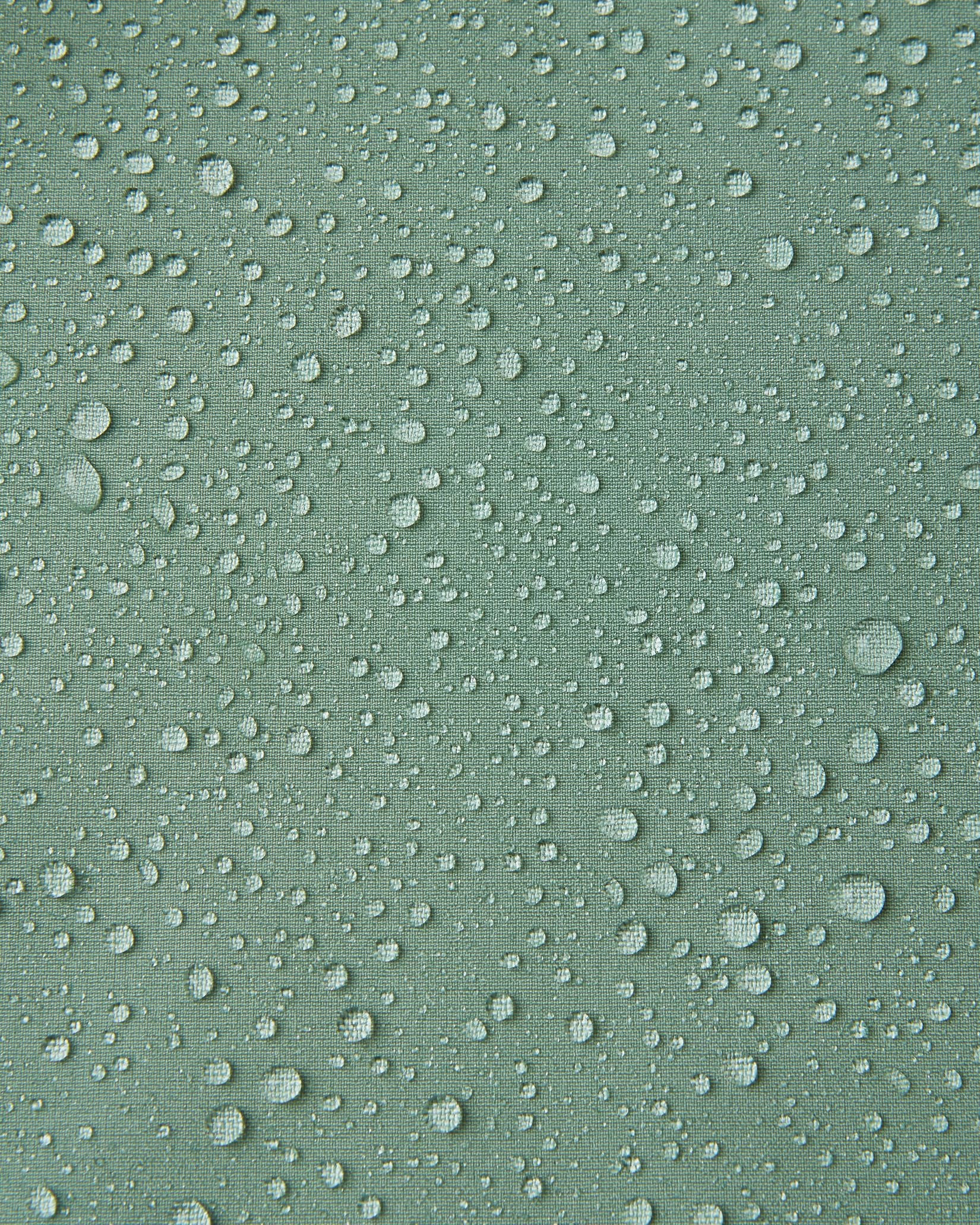Macro close-up of water droplets beading and rolling off the surface of the Reima Vantti kids' stone green softshell jacket, demonstrating the highly waterproof and dirt-repellent material.