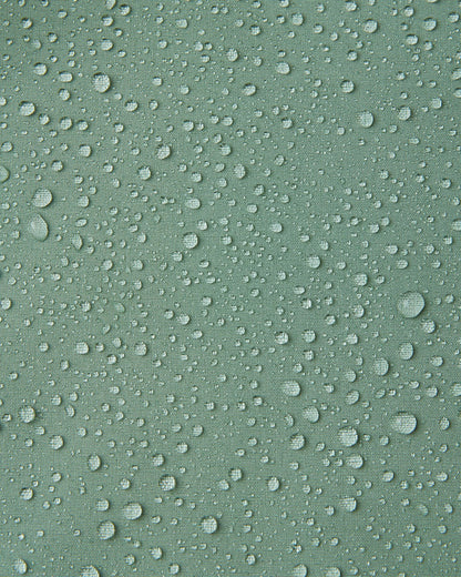 Macro close-up of water droplets beading and rolling off the surface of the Reima Vantti kids' stone green softshell jacket, demonstrating the highly waterproof and dirt-repellent material.