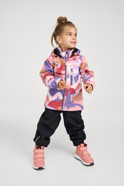 Lifestyle shot of a young girl wearing the rose blush Reima Vantti kids' waterproof softshell jacket paired with black rain pants and pink winter boots, demonstrating its comfortable fit for active outdoor play.