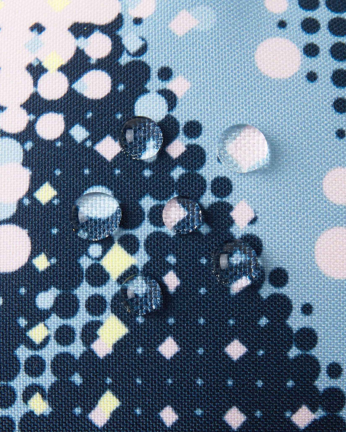 Macro close-up of water droplets actively beading and rolling off the frozen blue dot-patterned outer shell of the Reima Vanukko kids' ski mittens, demonstrating the high-performance waterproof and breathable technical fabric.