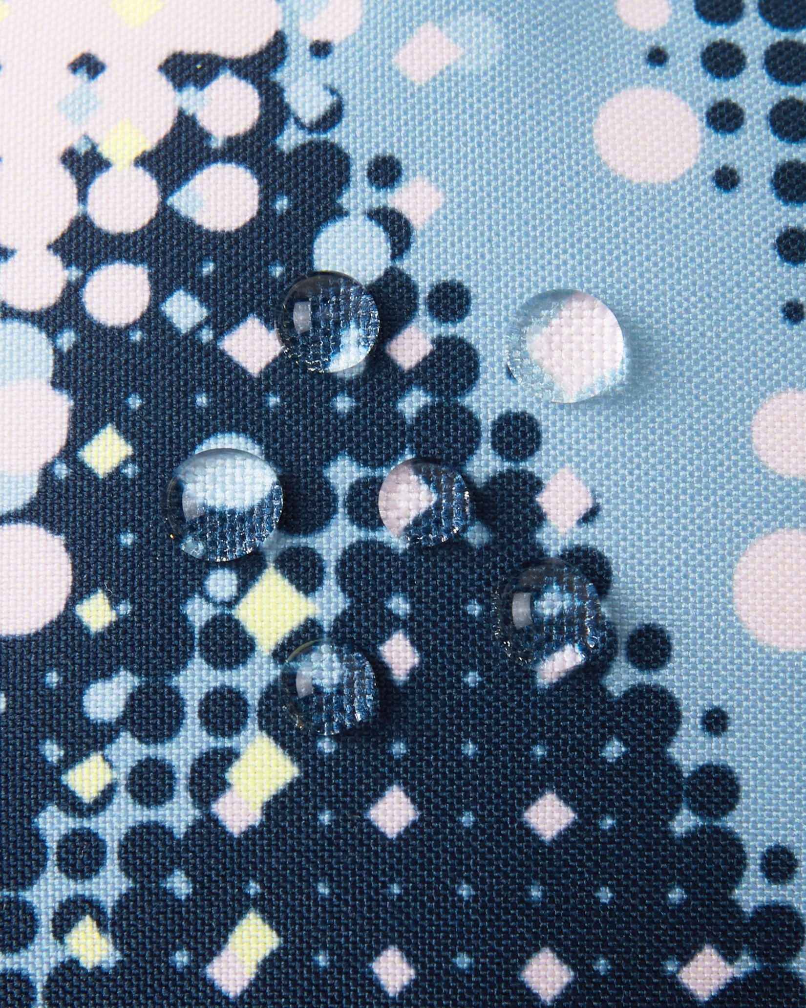 Macro close-up of water droplets actively beading and rolling off the frozen blue dot-patterned outer shell of the Reima Vanukko kids' ski mittens, demonstrating the high-performance waterproof and breathable technical fabric.