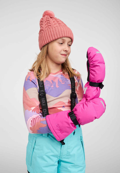 A young girl modeling the vibrant fuchsia Reima Vanukko kids' winter ski mittens, demonstrating the long protective cuffs and black palm grips. She is styled for winter sports in a pink knit beanie, patterned base layer, and light blue ski pants.