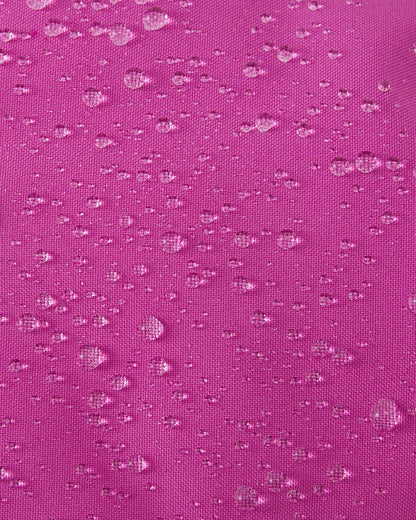 A macro close-up of the woven fuchsia fabric used on the Reima Vanukko kids' ski mittens, showing multiple water droplets beading on the surface to demonstrate its waterproof and dirt-repellent finish.
