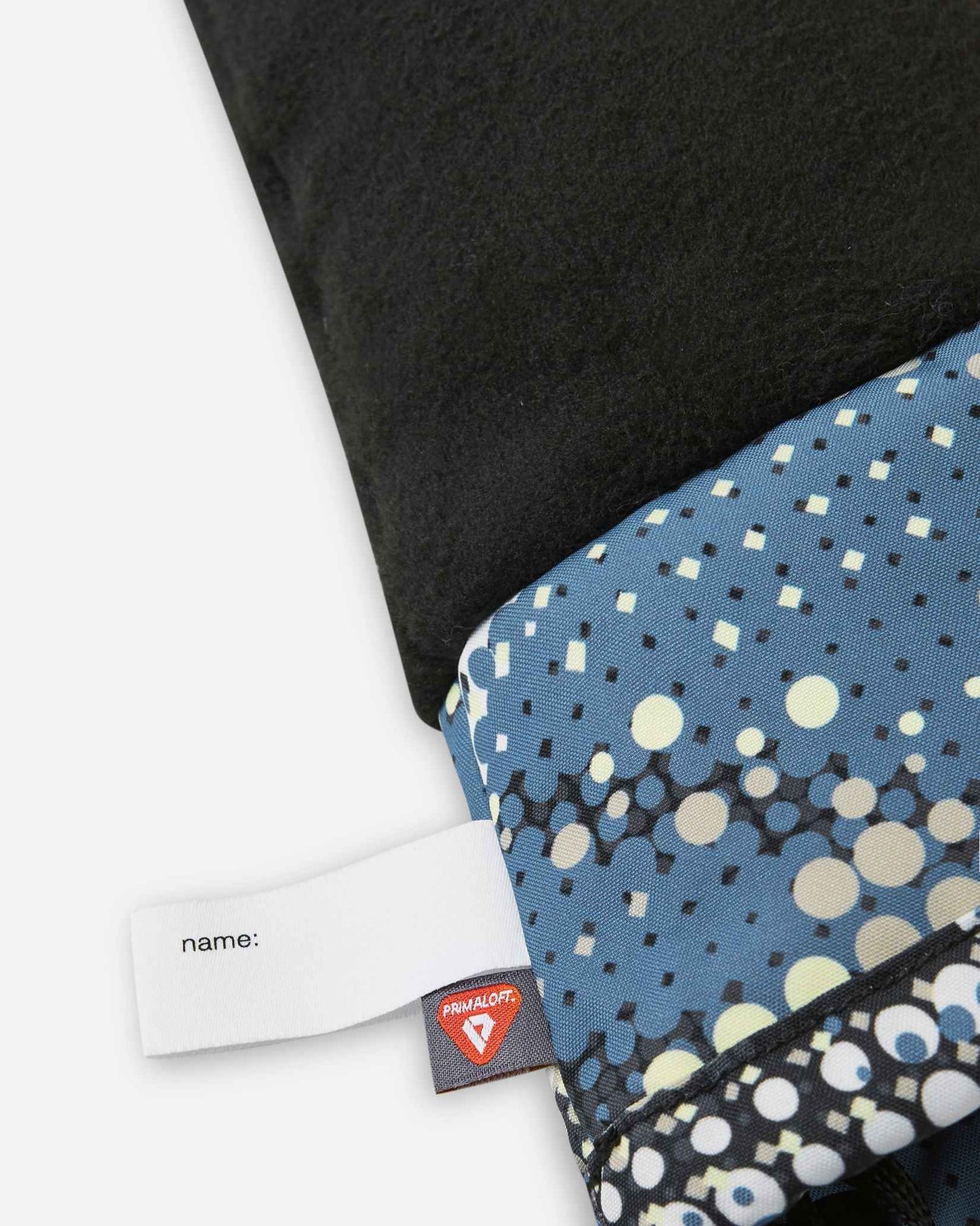 Close-up interior view of the soft black Reima Vanukko kids' ski mittens, showing the cozy thermal fleece lining, a customizable name tag, and a premium PrimaLoft insulation label indicating high-performance winter warmth.