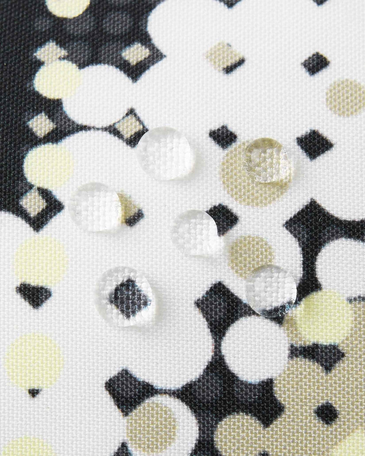 Macro close-up of water droplets actively beading and rolling off the soft black dot-patterned outer shell of the Reima Vanukko kids' ski mittens, demonstrating the highly effective waterproof and breathable technical membrane.