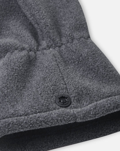 Close-up detail shot of the Reima Varmin kids' fleece gloves in black melange, highlighting the warm fleece texture, the gathered elastic wristband, and the practical snap button fastener used to clip the gloves together so they don't get lost.