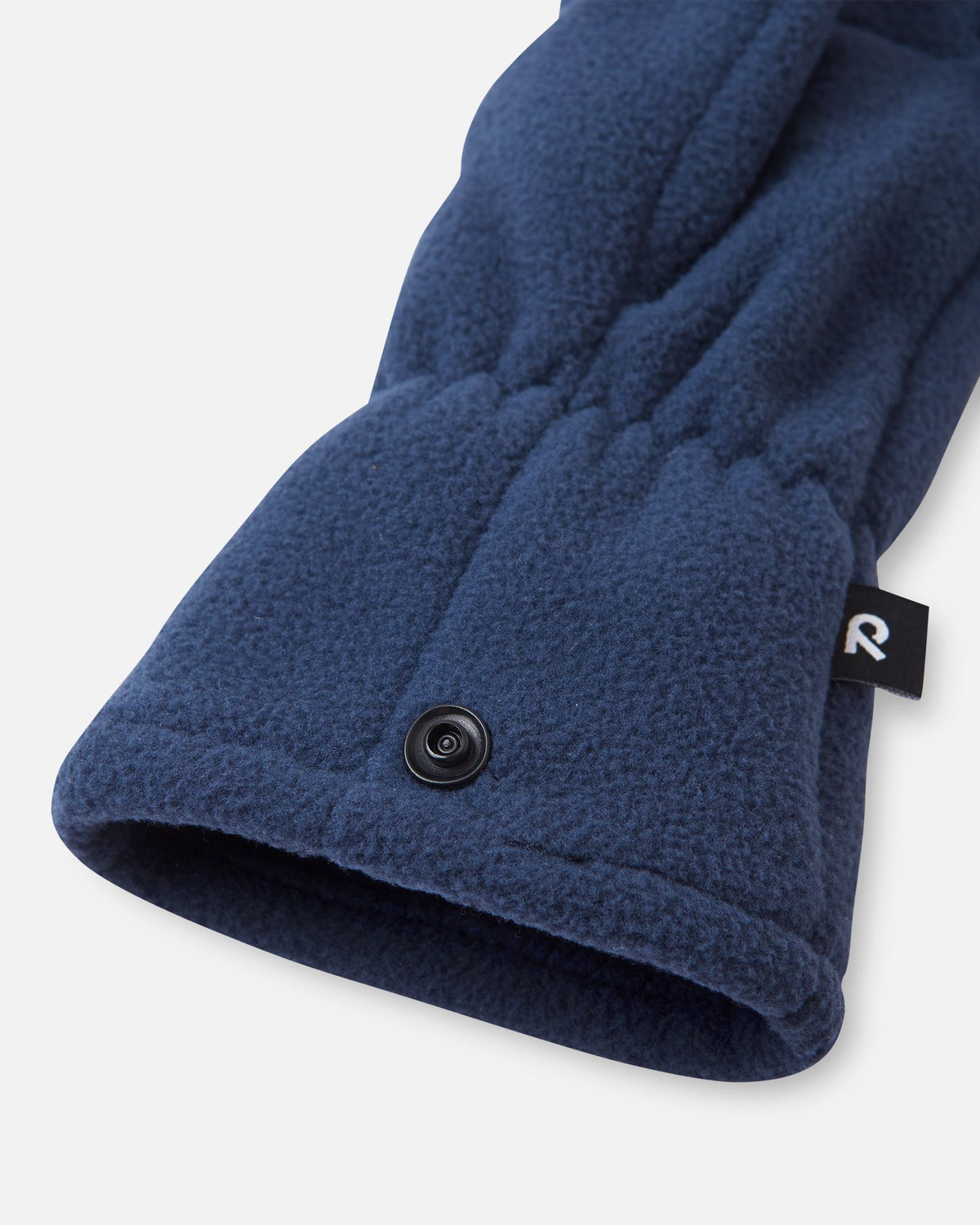 Close-up detail shot of the navy blue Reima Varmin kids' fleece gloves, highlighting the gathered elastic wrist, the black brand label, and the practical snap button used to clip the pair together when not in use.