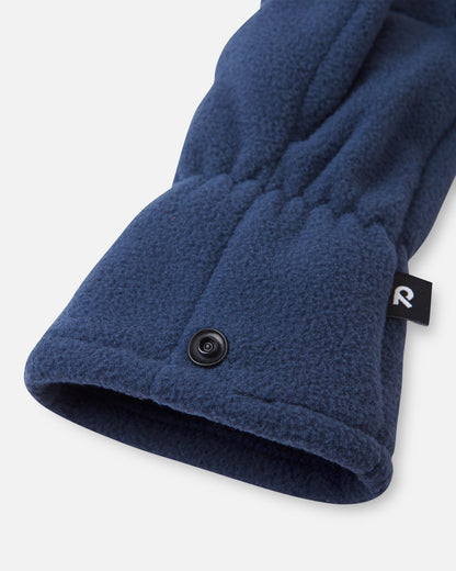 Close-up detail shot of the navy blue Reima Varmin kids' fleece gloves, highlighting the gathered elastic wrist, the black brand label, and the practical snap button used to clip the pair together when not in use.