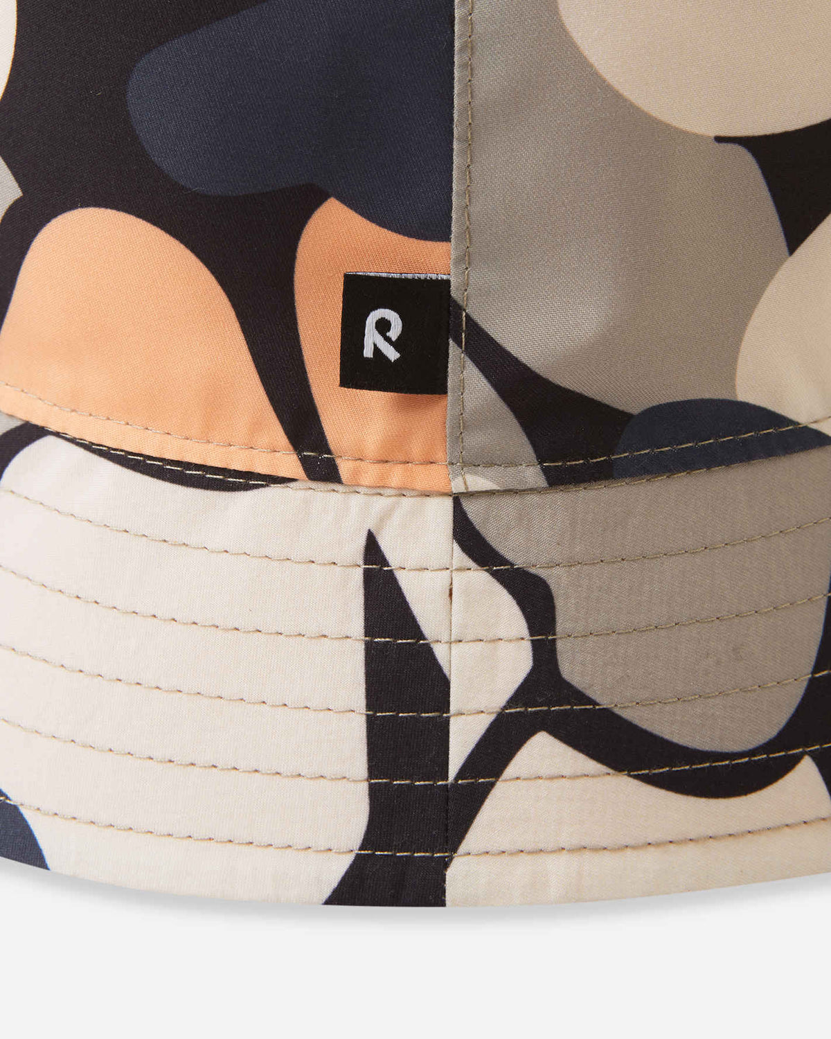 Detailed close-up of the Reima Viehe kids' UPF 50+ reversible sun hat in apricot, focusing on the durable sunproof fabric, floral print, and the black Reima logo tag.