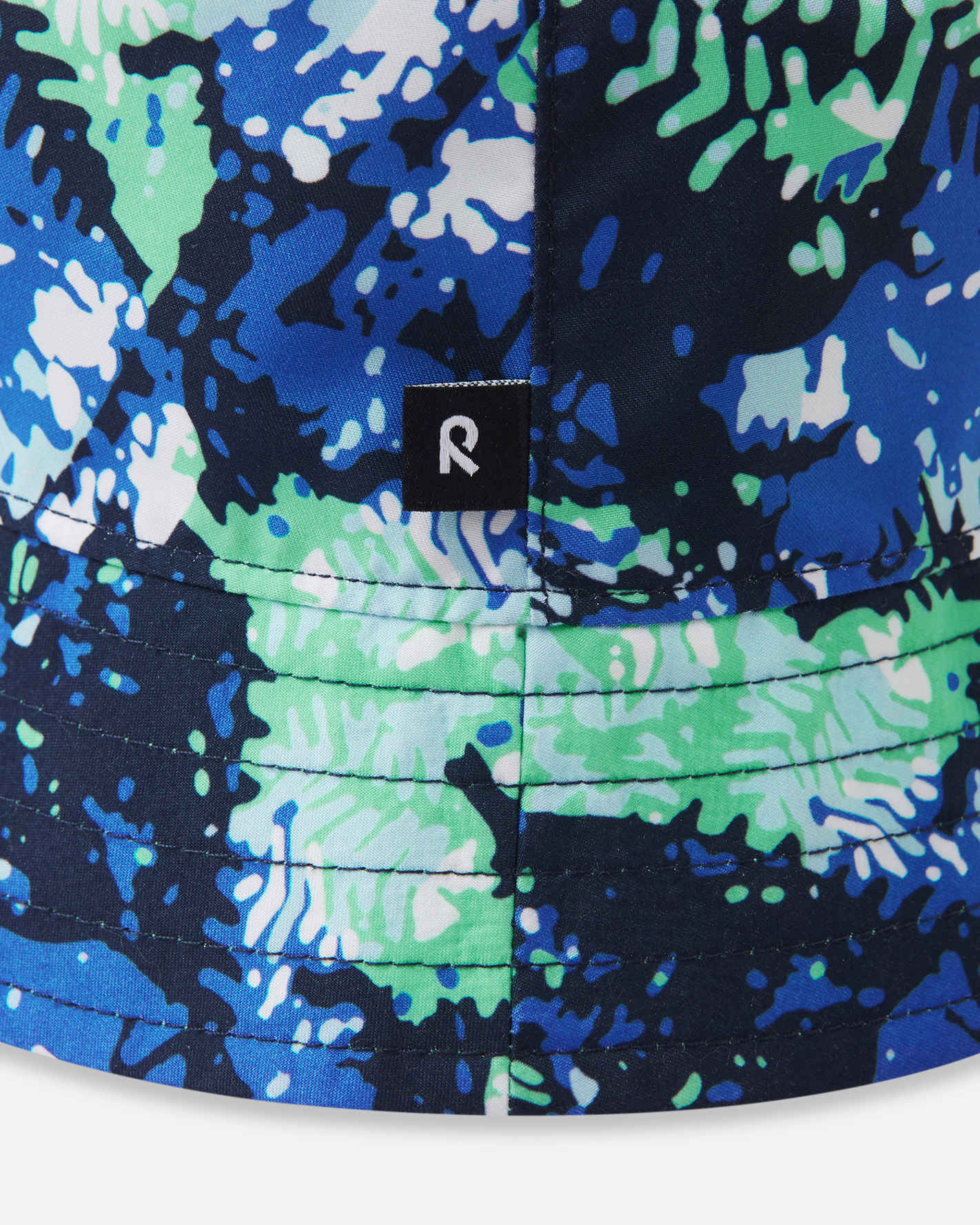 Close-up detail of the Reima Viehe kids' UPF 50+ reversible sun hat in fresh mint, highlighting the vibrant abstract pattern, neat brim stitching, and the signature black Reima logo tag.