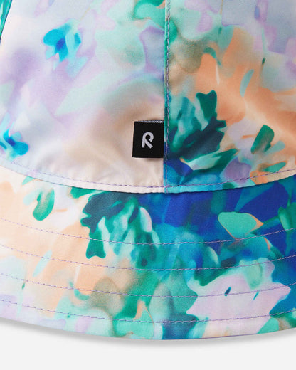 Close-up detail of the Reima Viiri kids' UPF 50+ reversible sunhat in fresh blue, showcasing the vibrant watercolor floral print and the signature Reima logo tag stitched on the brim.