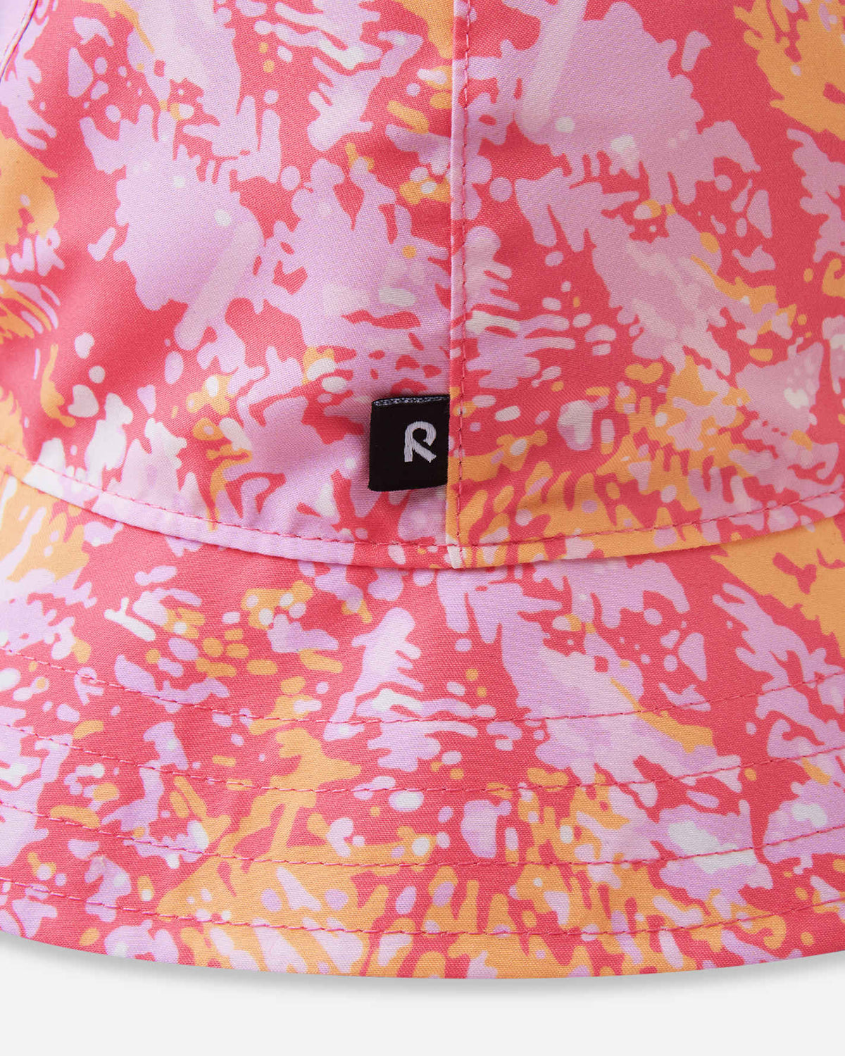 Detailed close-up of the Reima Viiri kids' UPF 50+ reversible sunhat in soft coral, highlighting the bright pink and orange abstract pattern, neat brim stitching, and the black Reima logo tag.