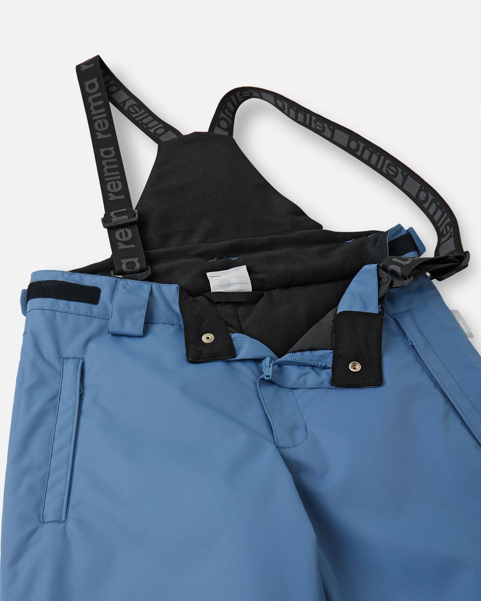 Close-up detail of the front waist on the blue ocean Reima Wingon kids' ski pants, showing the secure snap buttons, smooth zipper fly, soft inner lining, and the front attachment points for the adjustable suspenders.