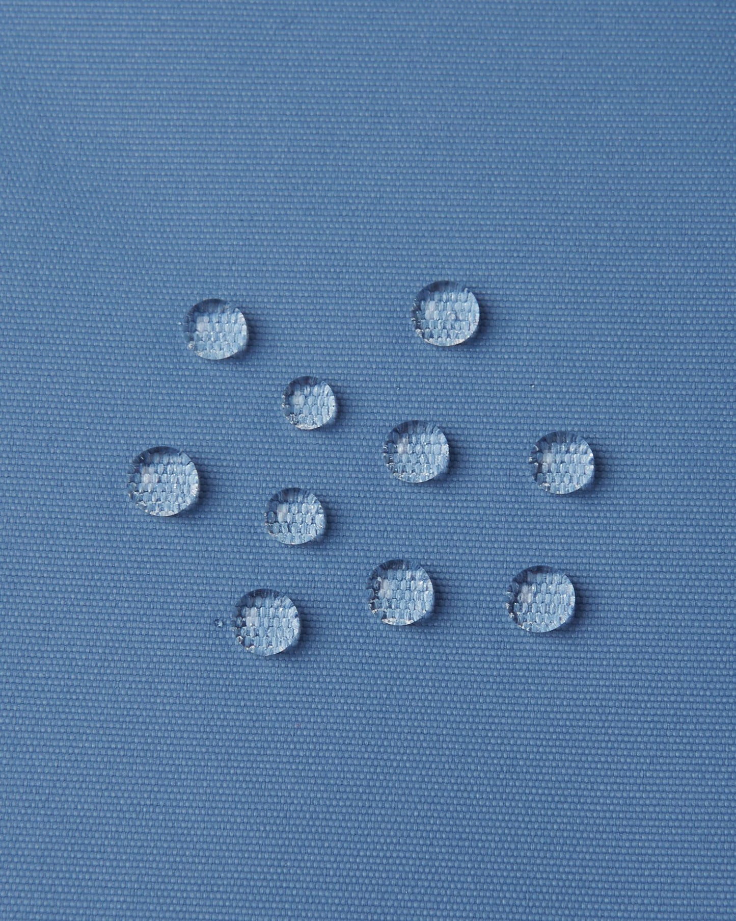 Macro close-up of water droplets actively beading and rolling off the blue ocean outer shell of the Reima Wingon kids' ski pants, visually highlighting the high-performance breathable and waterproof Reimatec technology.